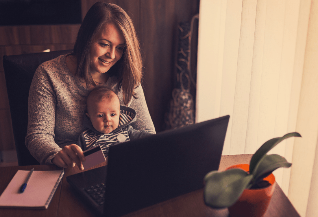 A smiling mother who is comfortably multitasking with her baby on her lap whilst shopping for health essentials, illustrating the convenience and ease of using an online pharmacy for busy parents. 